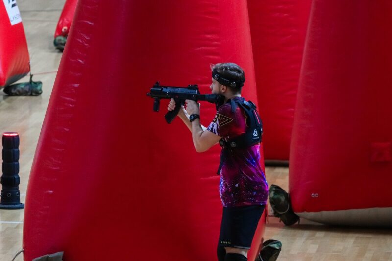 Боец LASERWAR прицеливается из-за красного препятствия.